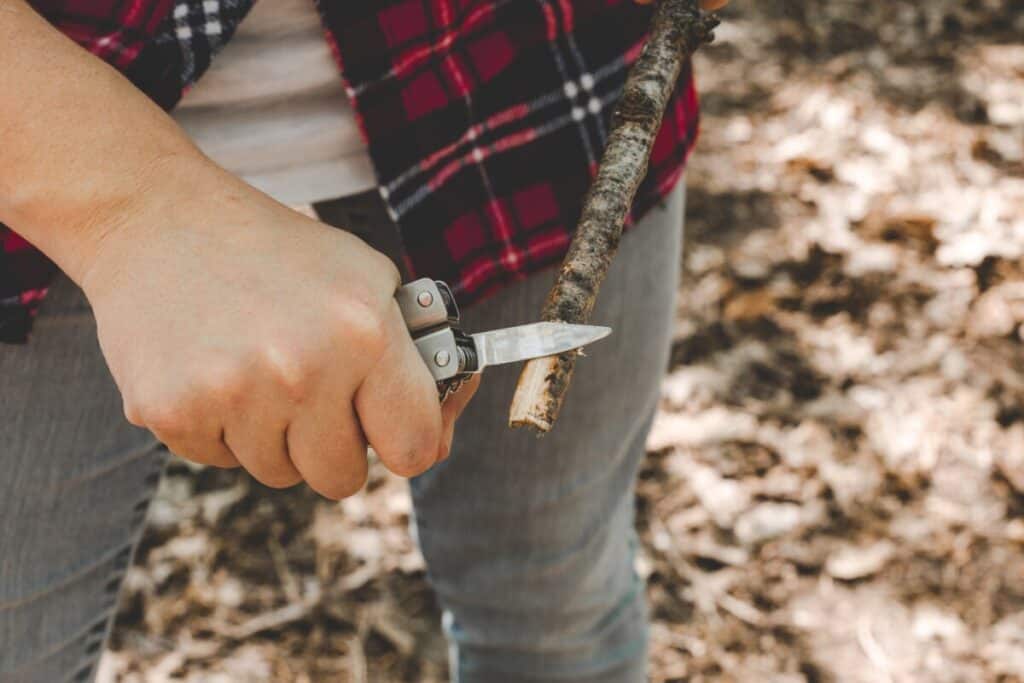 A folding pocket knife blade shaving thin curls off a wood stick
