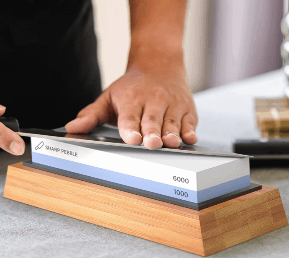 A blade drawn at a low angle across a two-sided sharpening stone marked 1000 and 6000 grit