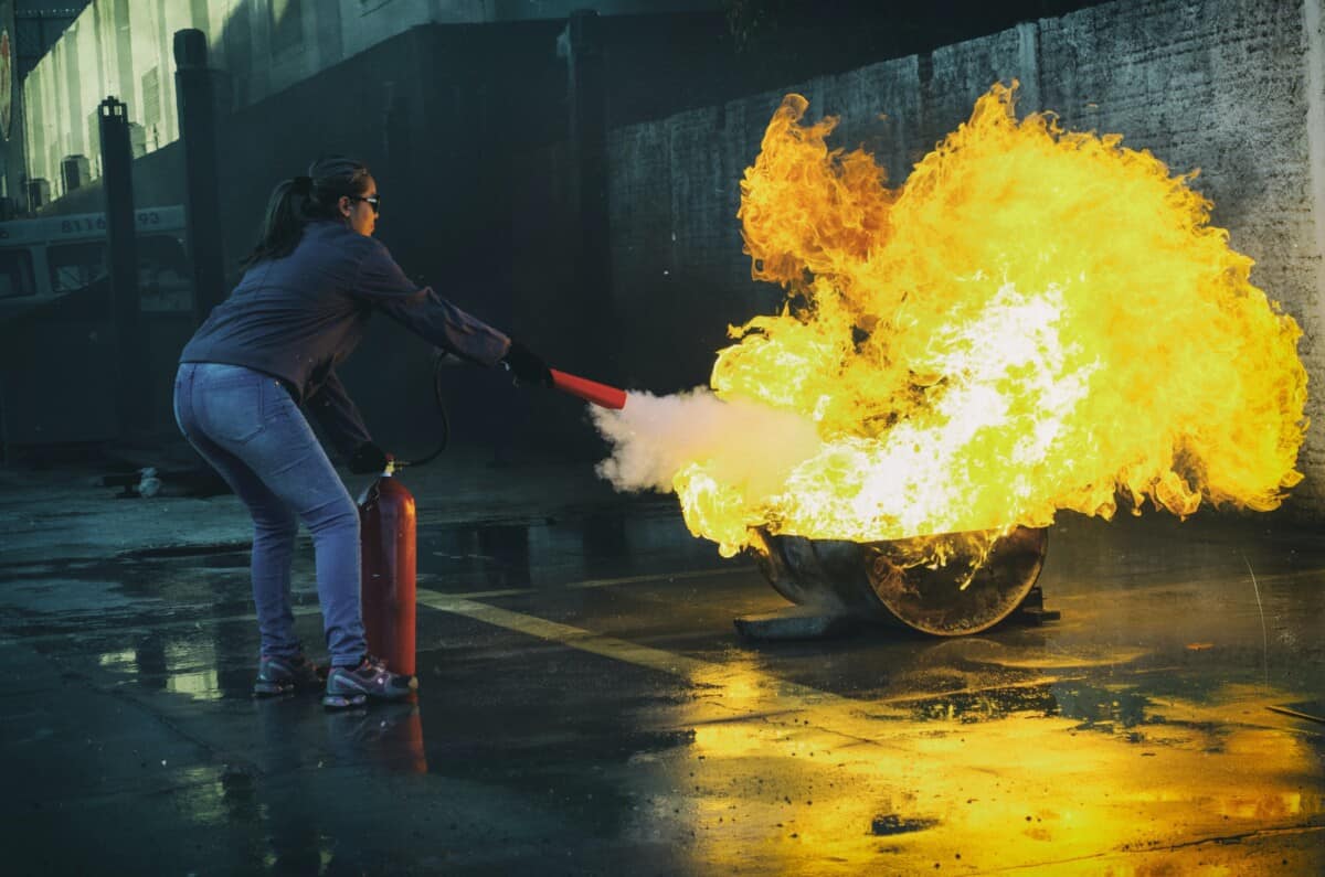 A person aiming a fire extinguisher's spray at the base of a large open flame during training