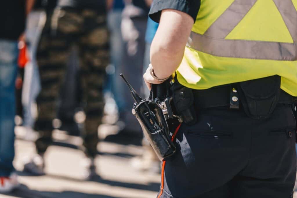 A portable radio clipped to a uniformed officer's duty belt next to other equipment pouches