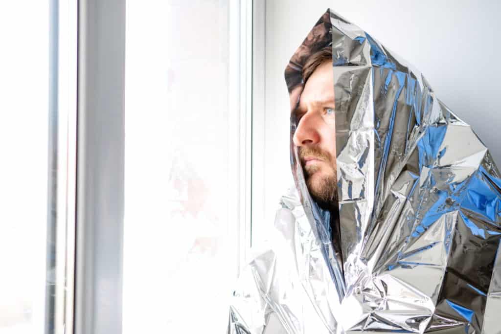 A man wrapped in a crinkled silver mylar emergency blanket pulled up over his head like a hood