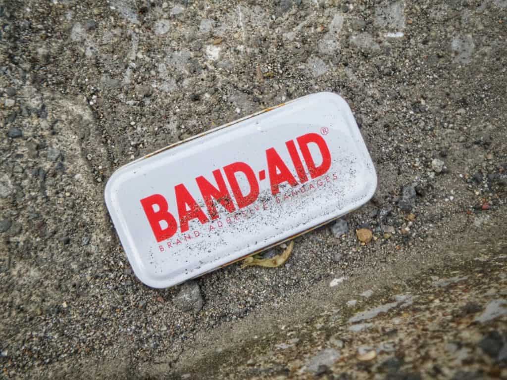 A rusted, dirt-covered vintage Band-Aid tin lying on gravel