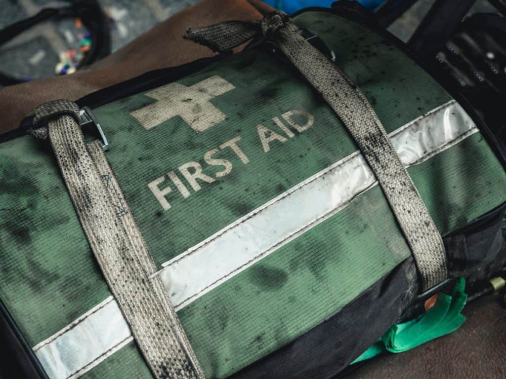A weathered green first aid duffel bag with faded lettering and grime on the carrying straps