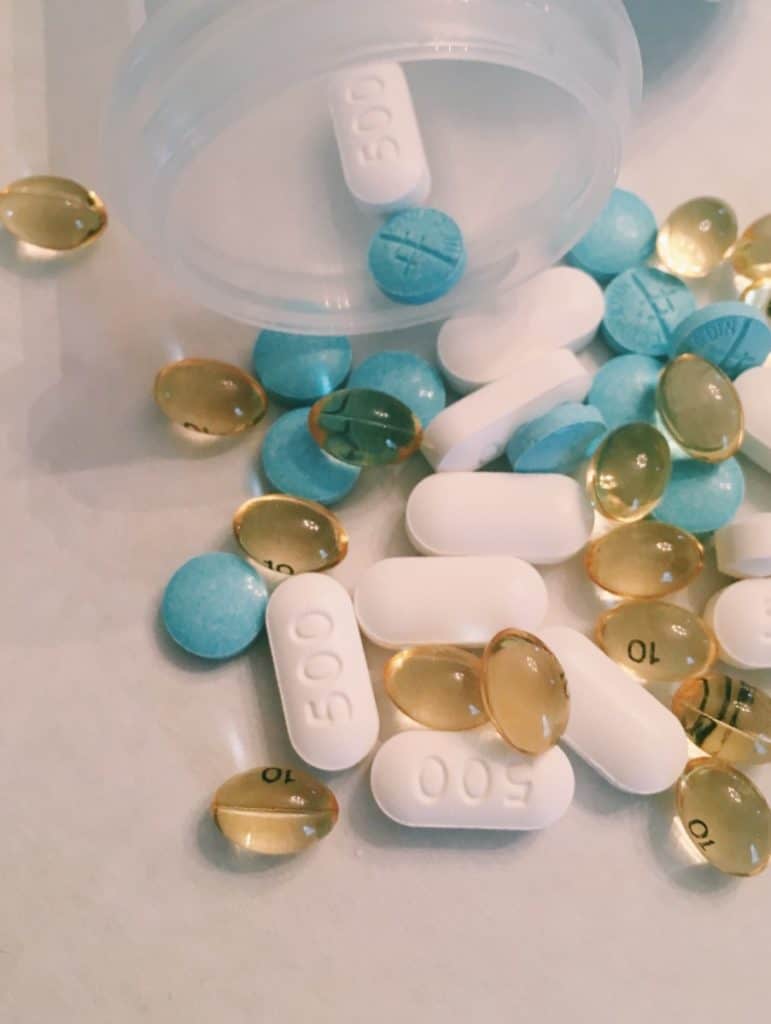 A mix of white, blue, and gold pills spilled out of an open pill bottle