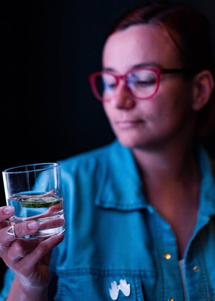 A woman examining a glass of water with a tablet dissolving at the bottom