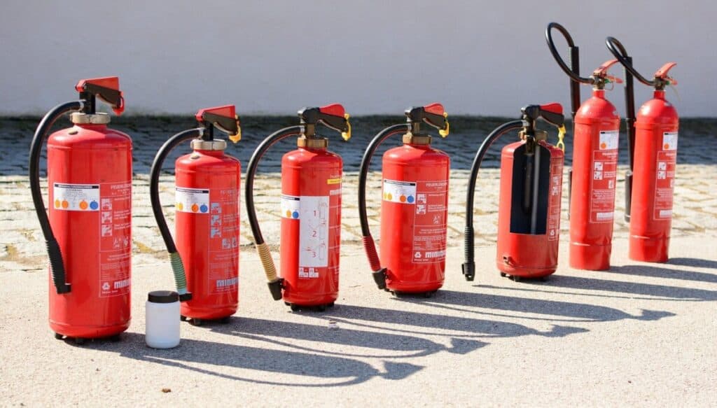 A row of seven fire extinguishers of different sizes and styles lined up on pavement