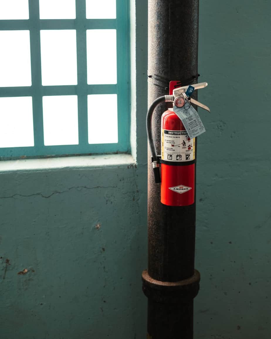 A red fire extinguisher zip-tied to a pipe with its white inspection tag hanging from the handle